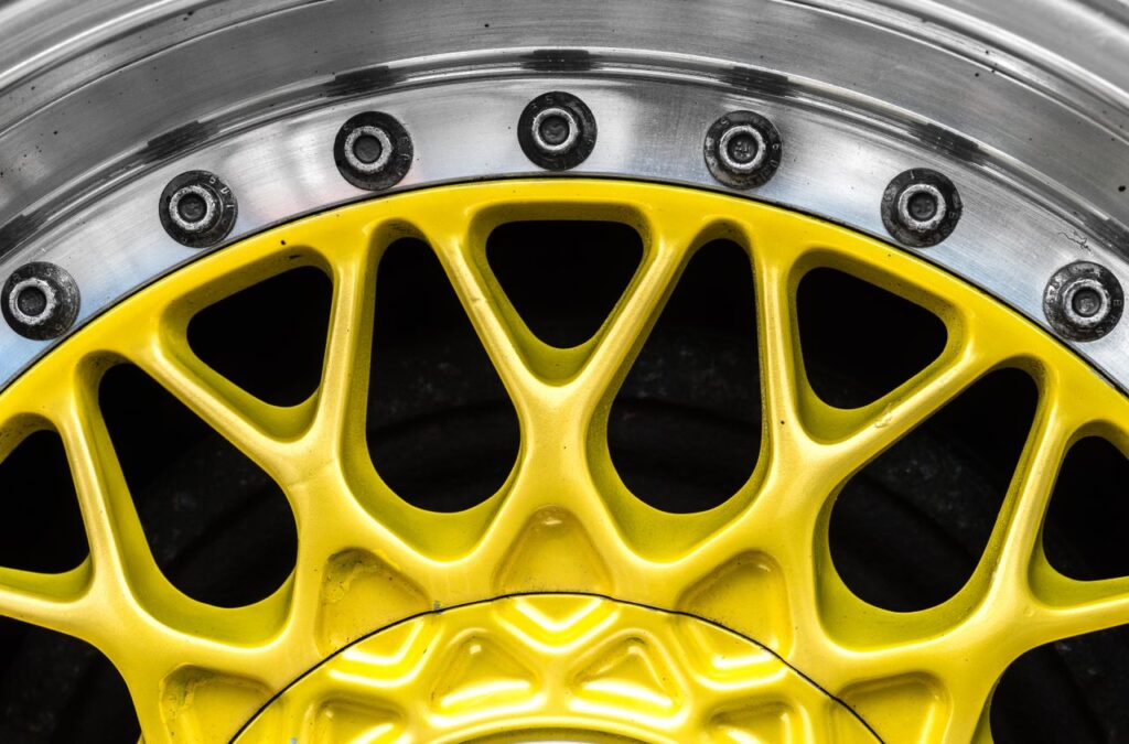 Extreme close-up of a bright yellow mesh car wheel rim with a polished silver outer lip and bolts.