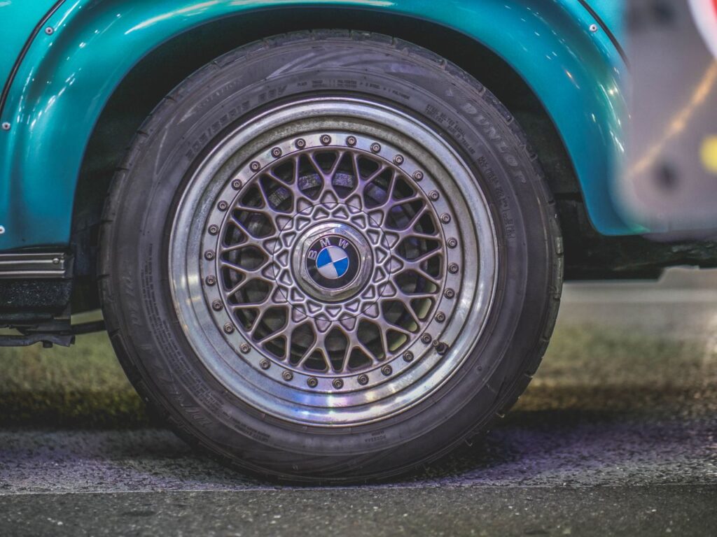 Side view of a classic silver mesh BMW wheel mounted on a teal blue car.