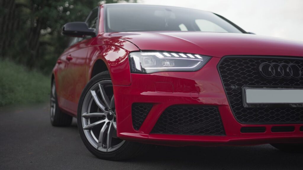 Front angle view of a red Audi sedan featuring a honeycomb grille and silver multi-spoke wheels.